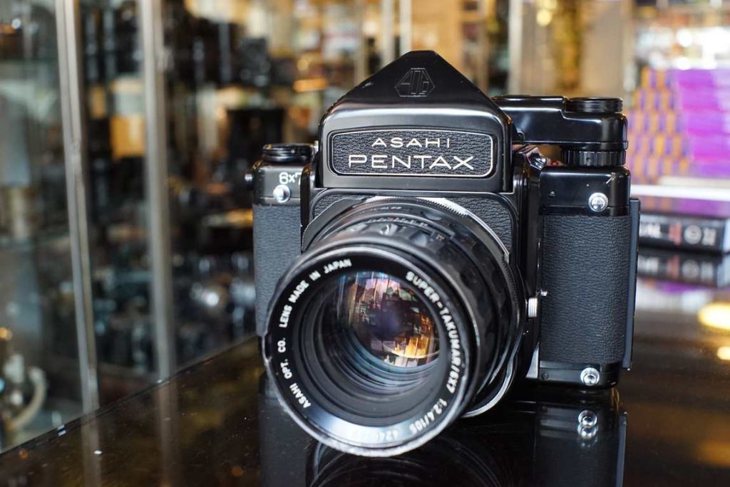This Pentax 6x7 comes with the holy grail of medium format lenses: the Super-Takumar/6x7 105mm F/2.4. This lens alone is one of many reasons why this system is so popular and sought after. The DOF rendition of this lens combined with the huge 6x7 negatives is a true unique look and one that can not be replicated with other systems. The Pentax 6x7 cameras are build like a tank, they basically are the same in operation as regular 35mm SLR cameras but just a bit bigger and heavier. Not your everyday walk around camera in terms of size and weight but certainly a really rewarding camera. You get 10 exposures out a roll of 120 film. This camera body has mirror lock up as well, which can come in handy for tripod work. The camera is fitted with a nice focusing screen and a metered prism, making it a joy and easier to use without external meter. br> This beautiful 67 kit recently was overhauled by our friend Alan from ACR. The camera received a big cleaning job, all mechanical systems were disassembled, cleaned, relubricated and put back togheter with the proper adjustments and calibration. The speeds run perfect again as well as the winding and cocking mechanisms. Lightseals have been replaced and the exterior of the camera was cleaned as well. The lens got its aperture calibrated and cleaned. The glass elements have been cleaned and the focus was afterwards calibrated on this body. There of course are some regular cosmetic usermarks on the body but this kit runs and shoots like new again.