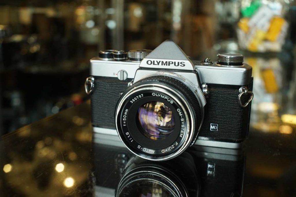 Olympus OM-1 in a good user condition. We have machine tested the speeds and meter and everything is perfectly usuable. 1s and 1/2s are a bit too slow, but these are speeds nobody uses anyway. The rest of the speeds are well within tolerance. Good accurate meter. New light seals have been installed. Some obvious usermarks on the camera but no big damages or dents that influence the operation. Nice user kit for people getting started in film, great lens and small overall system.