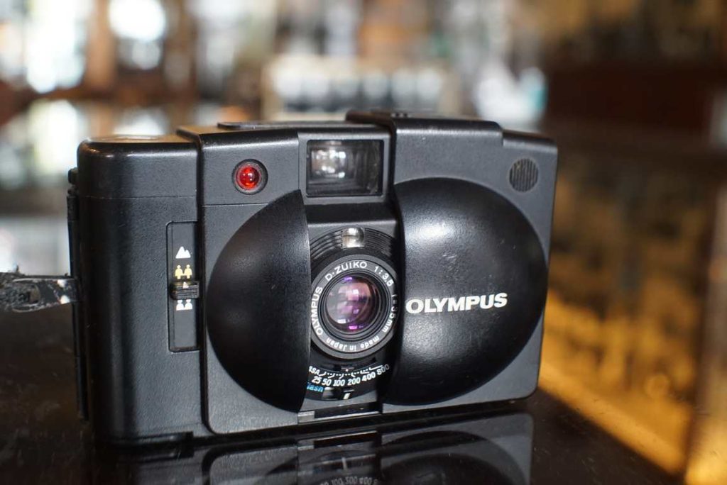 The Olympus XA2 is a cheaper alternative to the original XA, having a scale focus 35mm f/3.5 lens, but is still a nice small performer. The camera was checked over by us and works correctly and has a accurate shutter and lightmeter. Seals have been replaced. Flash also works just fine. Comes in clamshell case with wrist strap.this item comes with a 2 month limited warranty* (in case the item can not be repaired we will provide a similar item or different solution)