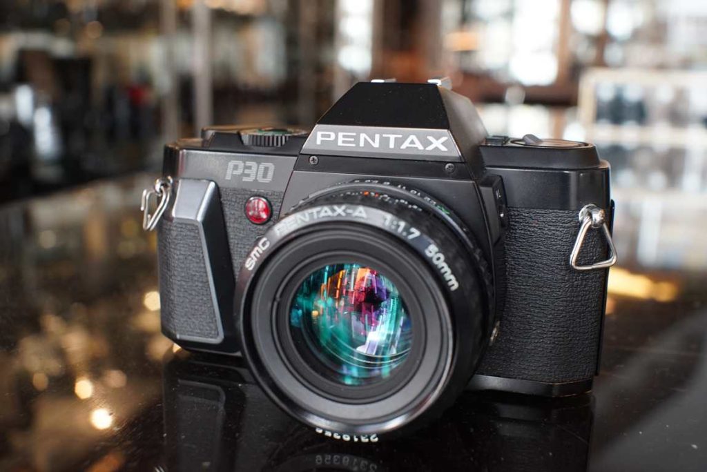 The Pentax P30 is a budget friendly starter camera with both manual and program exposure modes. The camera is still in good shape with some regular wear from previous use. The top plate has a dent near the counter but does not harm functionality. Shutter speeds are all accurate and the lightmeter also works within margin. Light seals are still in good shape and didnt need replacement. The SMC-A 50mm f/1.7 lens has smooth focus and aperture works correctly. Optics look good without fungus or haze.this item comes with a 3 month limited warranty