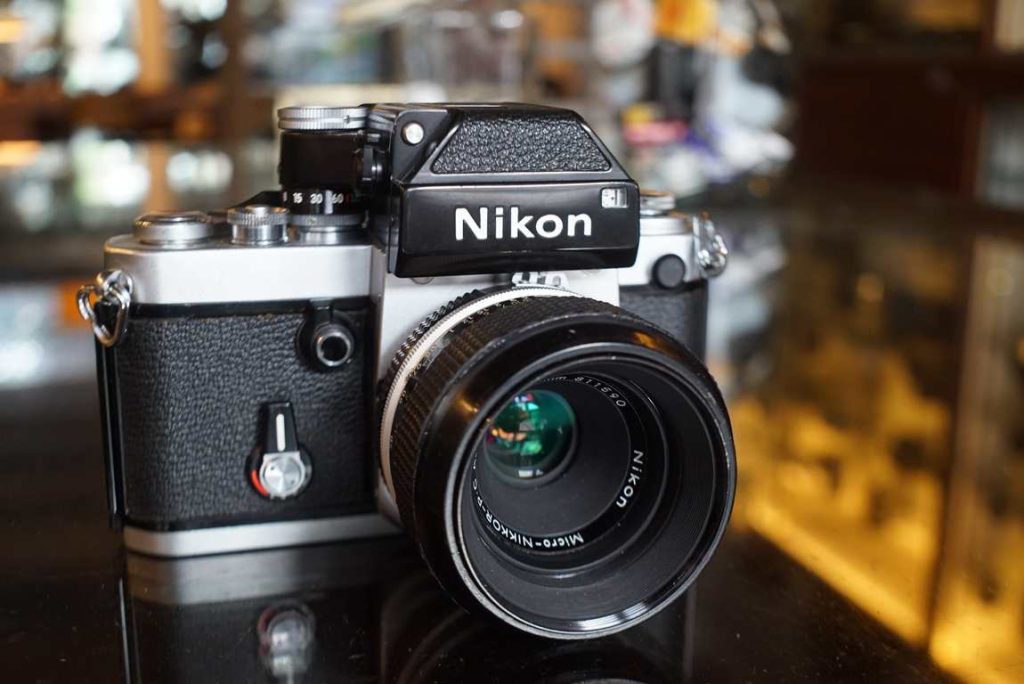 Nikon F2 with DP-1 Photomic finder with a factory AI converted Micro-Nikkor 55mm f/3.5 lens as a standard lens. The kit has some regular wear which is to be expected from a professional grade camera. It is free of dents however, mostly some wear on the bottom plate. The shutter speeds are all within margin, as it has received a small tuneup from our inhouse technicians. The lightmeter works and is accurate, verified by our testing equipment. The Micro-Nikkor 55mm f/3.5 is in good shape with some regular wear. Focus turns smoothly and can go up to 1:2 magnification without extension tubes. Aperture works correctly and goes blades are free of oil. Optics are in nice shape without haze or fungus. Nice all mechanical kit.this item comes with a 3 month limited warranty