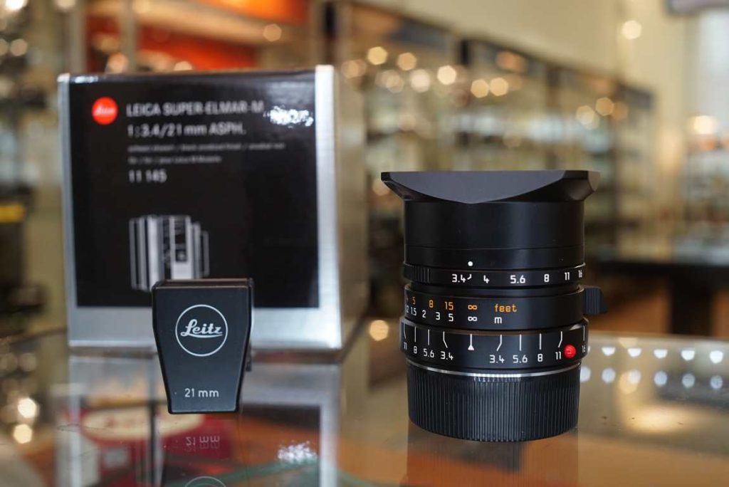 Modern production Leica Super-Elmar-M 21mm f/3.4 ASPH, including a Leica 12008 21mm finder. The lens was introduced in 2011 and this one is likely from around 2012. The lens looks like it was never even used, and comes complete in it's original inner and outer box. Focus turns smoothly and the aperture ring also turns smoothly like it should. Optics are in perfect shape without remarks. The 12465 lens hood cap is missing but replacements are easily found online or you can also 3d print one. The 21mm finder is in good shape with good view through it and comes with leather storage case. Lens comes with leather storage case. 6 bit codedthis item comes with a 3 month limited warranty